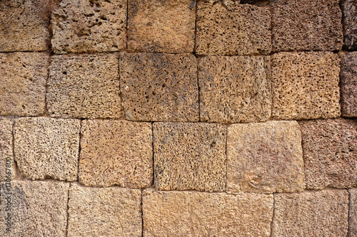 yellow stone wall of an ancient temple with irregular square porous volcano stone cubes - the holes and the shape of the volcanic blocks create an individual pattern. 