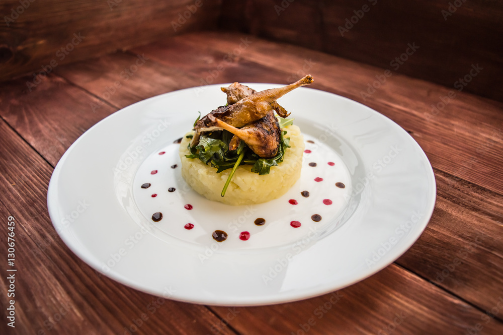 Roasted quail on a bed with mashed potatoes, rocket leaves and berry sauce. white plate wooden rustic background. Top view. Close-up Roasted quail on a bed with mashed potatoes, rocket leaves and berry sauce. white plate wooden rustic background. Top view. Close-up