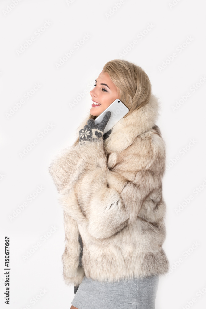 the young woman in a fur coat stands and speaks by phone and smi the young woman in a fur coat stands and speaks by phone and smi