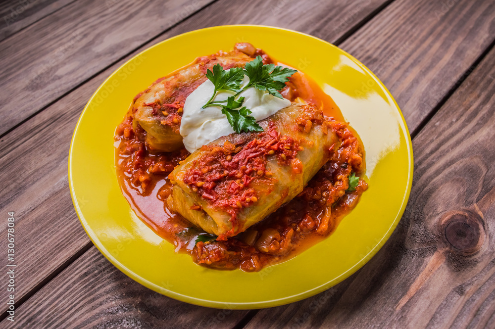 Dinner with cabbage rolls in tomato sauce decorated parsley. Wooden rustic background. Top view. Close-up Dinner with cabbage rolls in tomato sauce decorated parsley. Wooden rustic background. Top view. Close-up