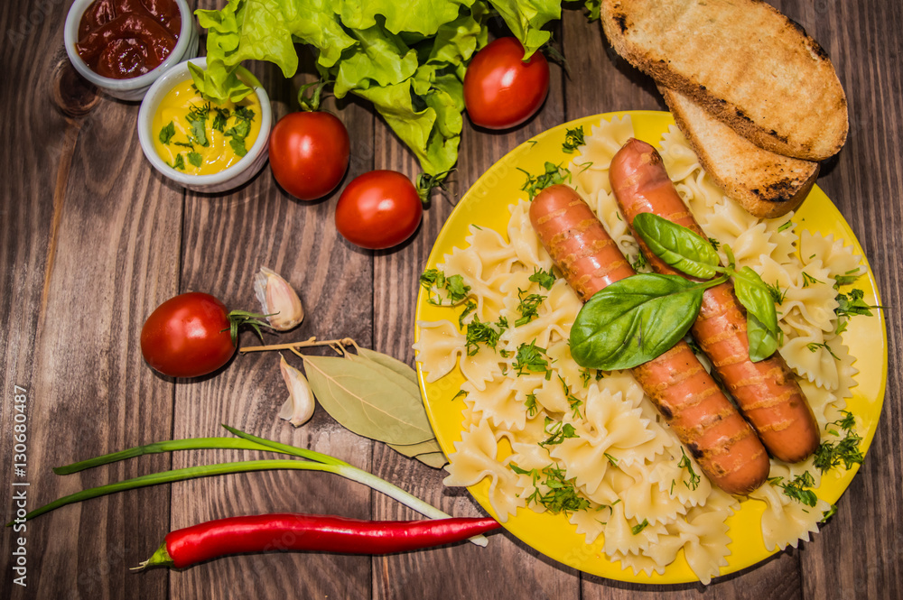 Grilled sausage with pasta, slices of bread, herbs and cherry tomatoes. Top view. On a wooden rustic brown background. Close-up Grilled sausage with pasta, slices of bread, herbs and cherry tomatoes. Top view. On a wooden rustic brown background. Close-up