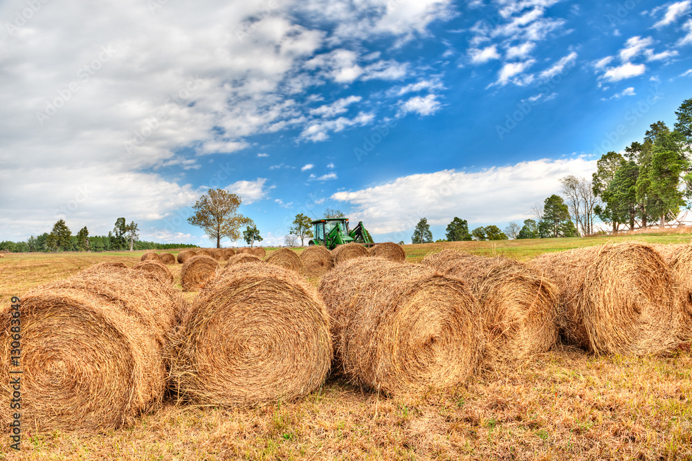 Hay roll bales with tractor on countryside field