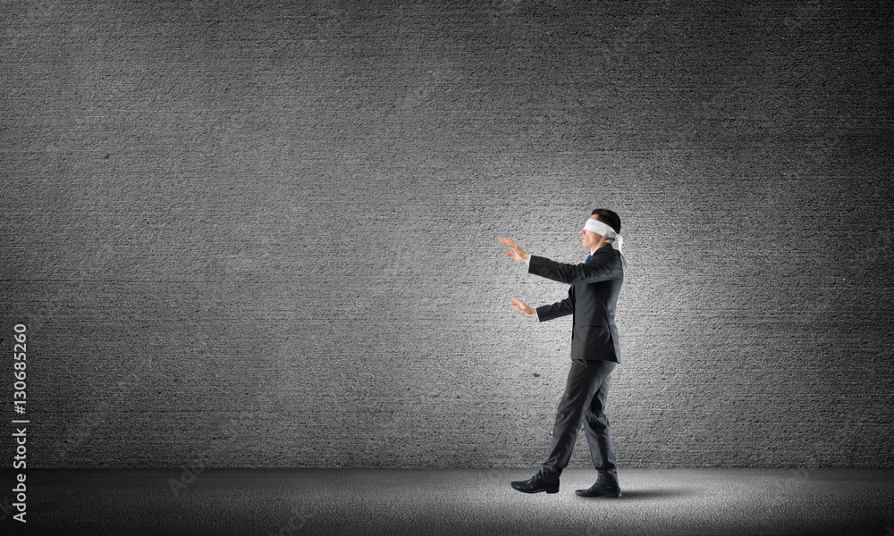 Business concept of risk with businessman wearing blindfold in empty concrete room Business concept of risk with businessman wearing blindfold in empty concrete room