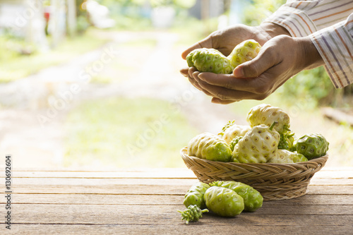  Noni fruit and noni basket on wooden table.And noni in his hand.Zoom in photo