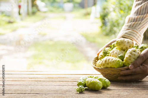 Noni fruit on wooden table.And noni basket in his hand.Zoom in photo