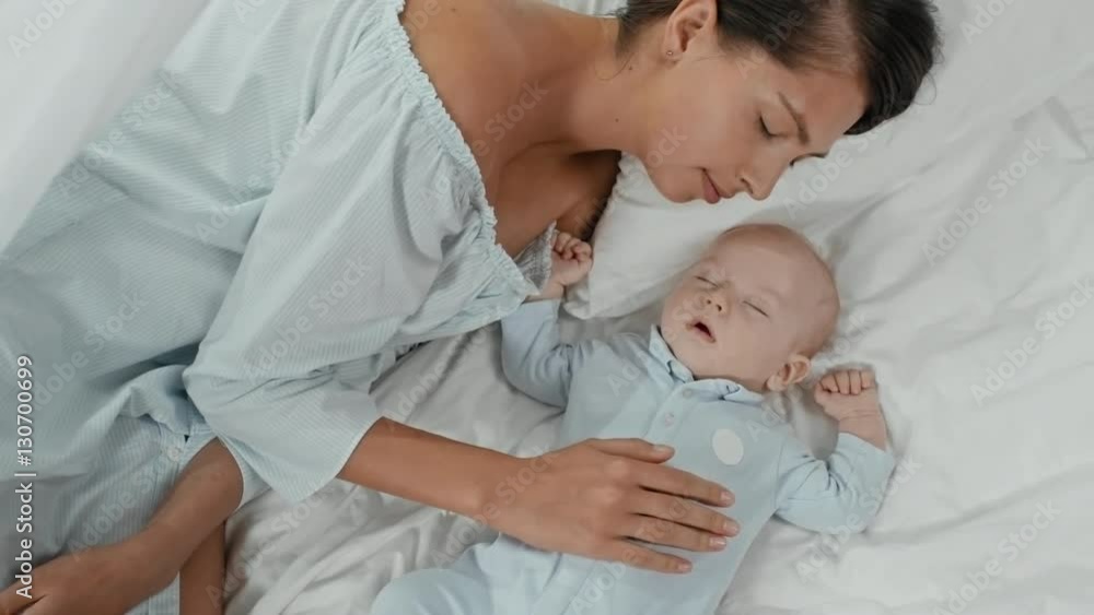 Top view of loving mother lying with her eyes closed in bed and caressing her sleeping infant boy Top view of loving mother lying with her eyes closed in bed and caressing her sleeping infant boy
