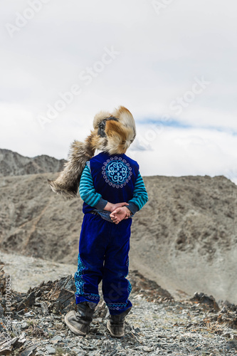 cute boy portrait of Kazak family : Mongolian is wearing fox hat .on mountain,.