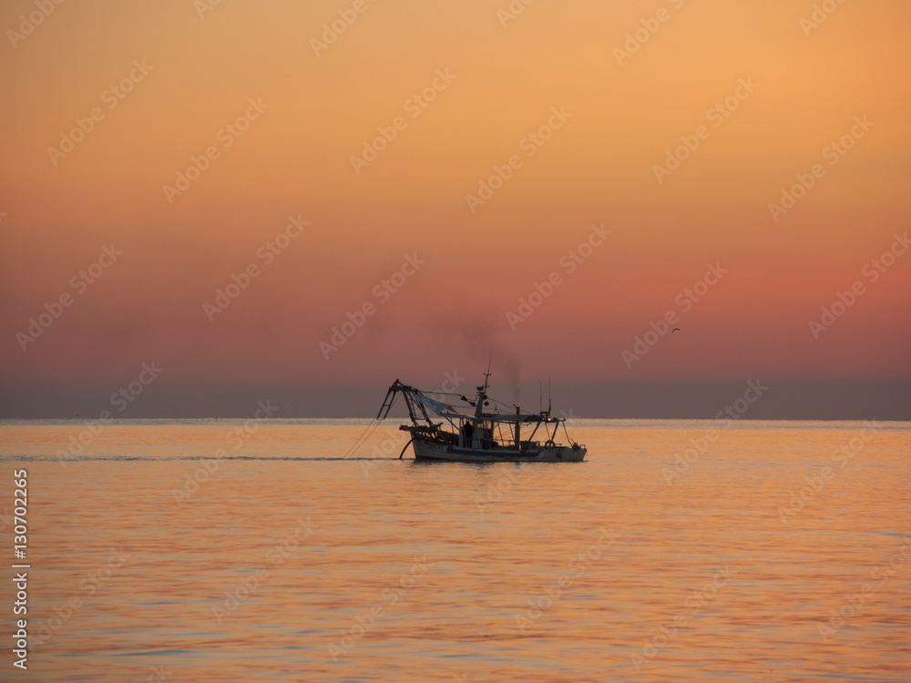 Fishing boats pull their nets at the sunrise. Adriatic cost. Emilia Romagna. Italy.