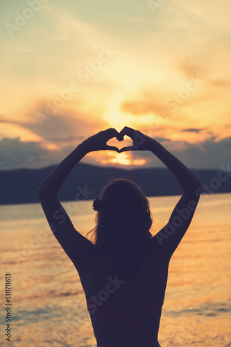 Girl holding a heart shape for the ocean / sea. 