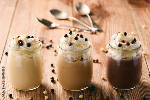 Milk, toffee and chocolate pudding with whipped cream on brown wooden background. photo
