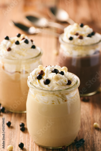 Milk, toffee and chocolate pudding with whipped cream on brown wooden background.