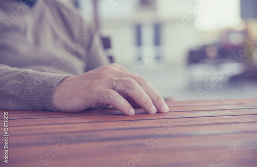 young man's hand with a gold wedding ring on wooden table,blurred background