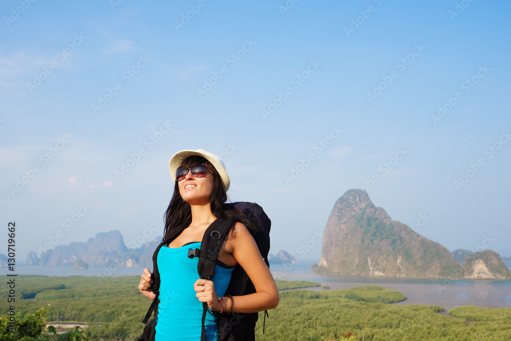 Happy hiker with backpack standing on top of the mountain and enjoying valley view