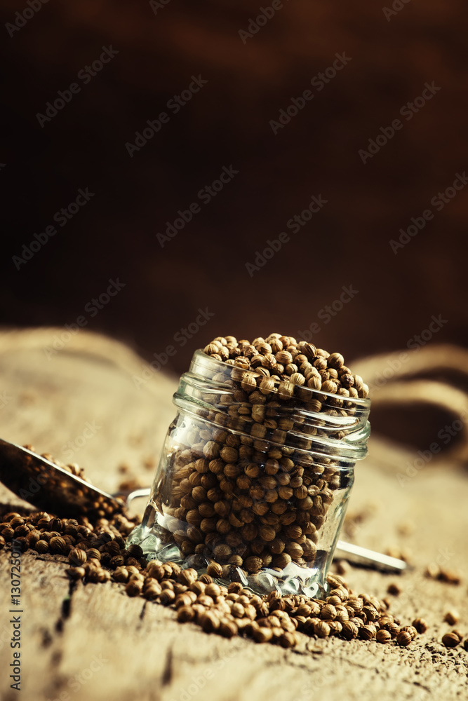 Fototapeta premium Coriander seeds in jar, rustic style, selective focus