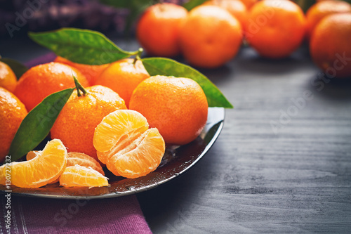 Fresh clementines with leaves served on plate, on black wooden table. Copy space photo
