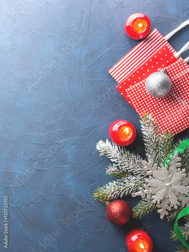 Dark christmas background with red candle, fir tree branches, gift bags and baubles. Top view copy space
