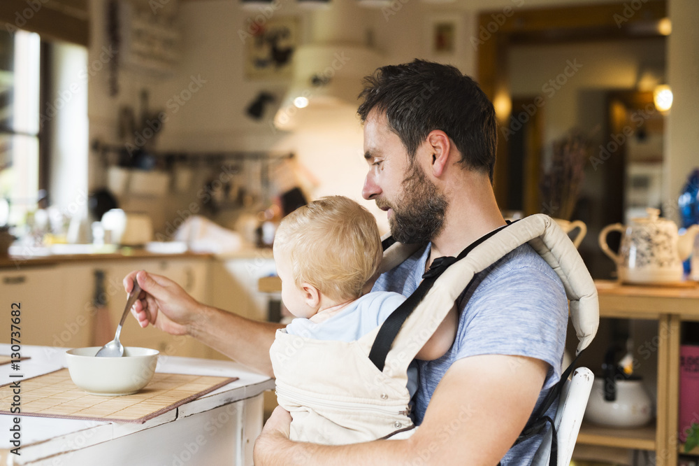 Father feeding baby in baby carrier Father feeding baby in baby carrier
