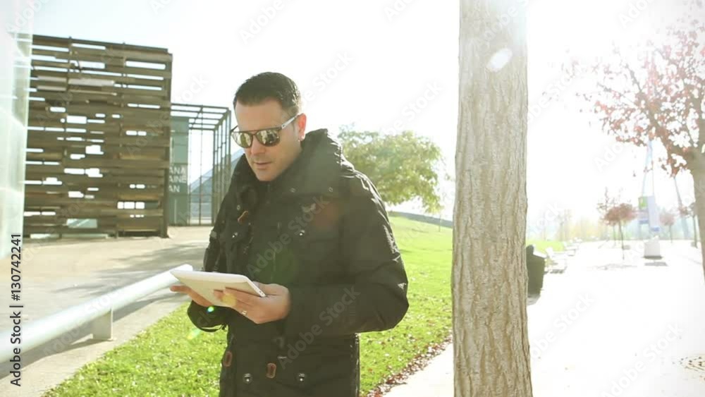 Hombre caminando en la calle con la tablet. Estilo de vida y vida moderna, paisaje urbano. Concepto de tecnología y comunicación. Rayo de sol y puesta de sol