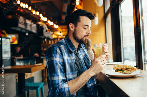 Young man is sitting in the restaurant and taste a warm drink.