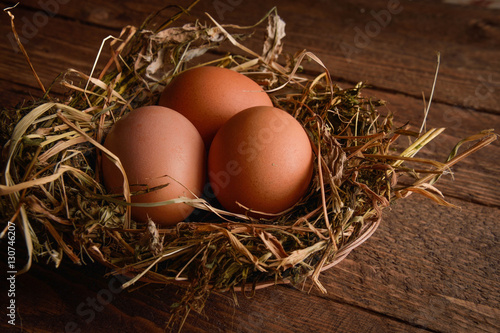 Chicken eggs in a wicker straw nest on wooden background