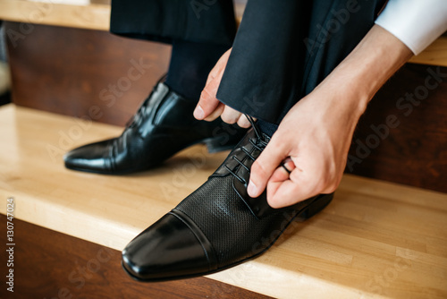 Man ties the laces on his polished shoes. Business formal dress style. Official event, perhaps a wedding. Cropped image