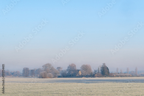 Dutch rural winter landscape with frozen meadow and a farm