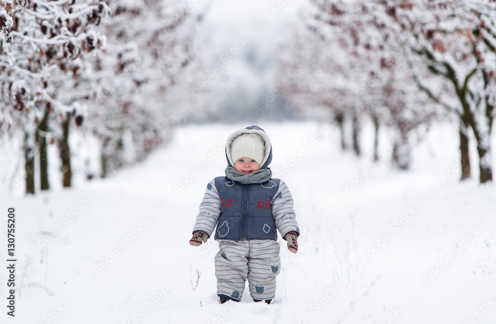Little kid in snowsuit, hat and scarf, walking through a snowy path