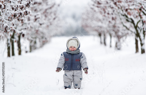 Obraz na płótnie Little kid in snowsuit, hat and scarf, walking through a snowy path w salonie