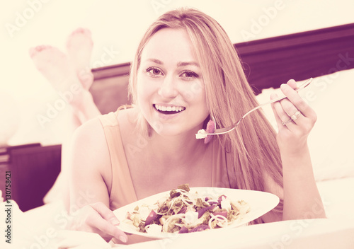 Woman lying in the bed and eating salad