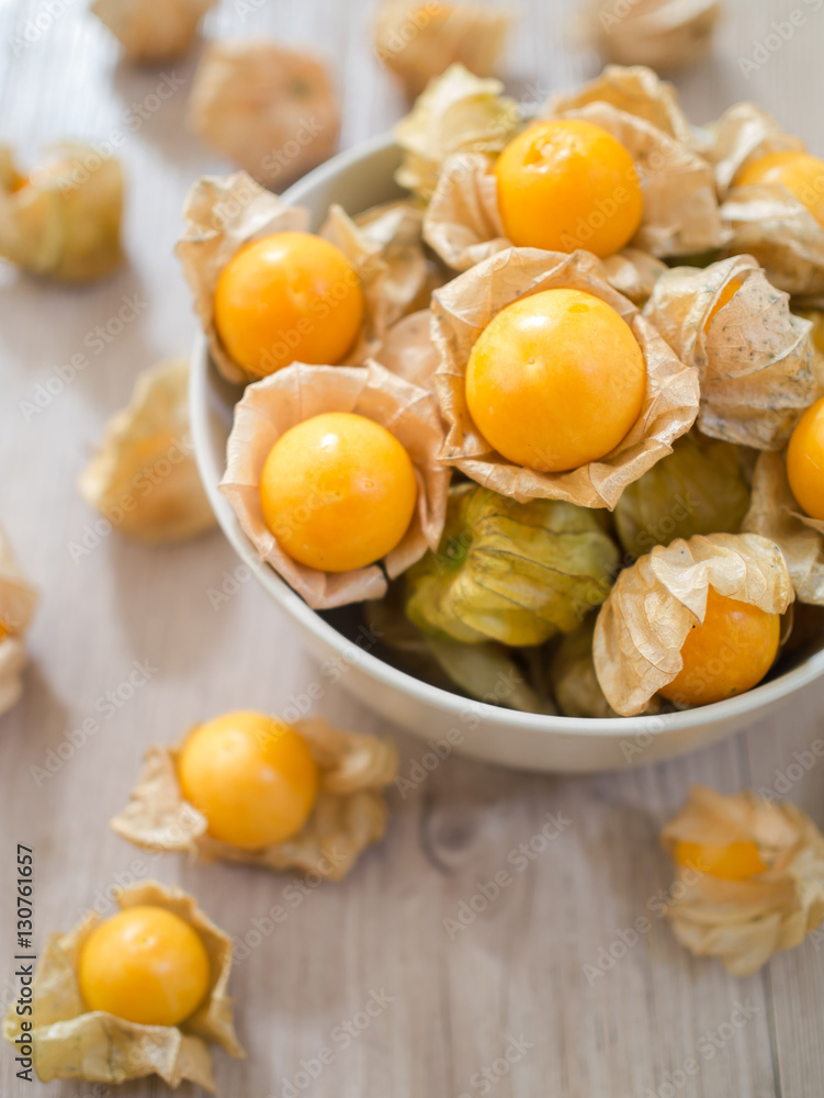 Fresh Cape gooseberry in white bowl and on wooden board Fresh Cape gooseberry in white bowl and on wooden board