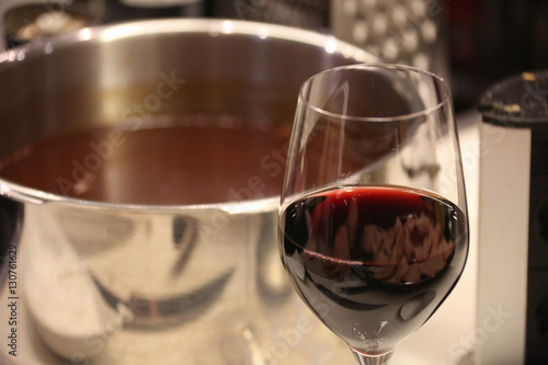 a dark gravy in a pot of stainless steel on a ceramic glass cooktop with a glass of wine in front of it