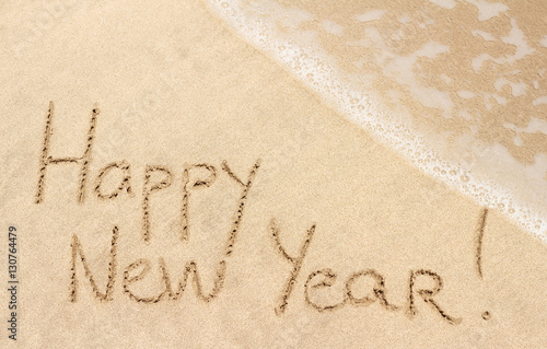 Happy New Year handwritten on sandy beach with ocean wave on background