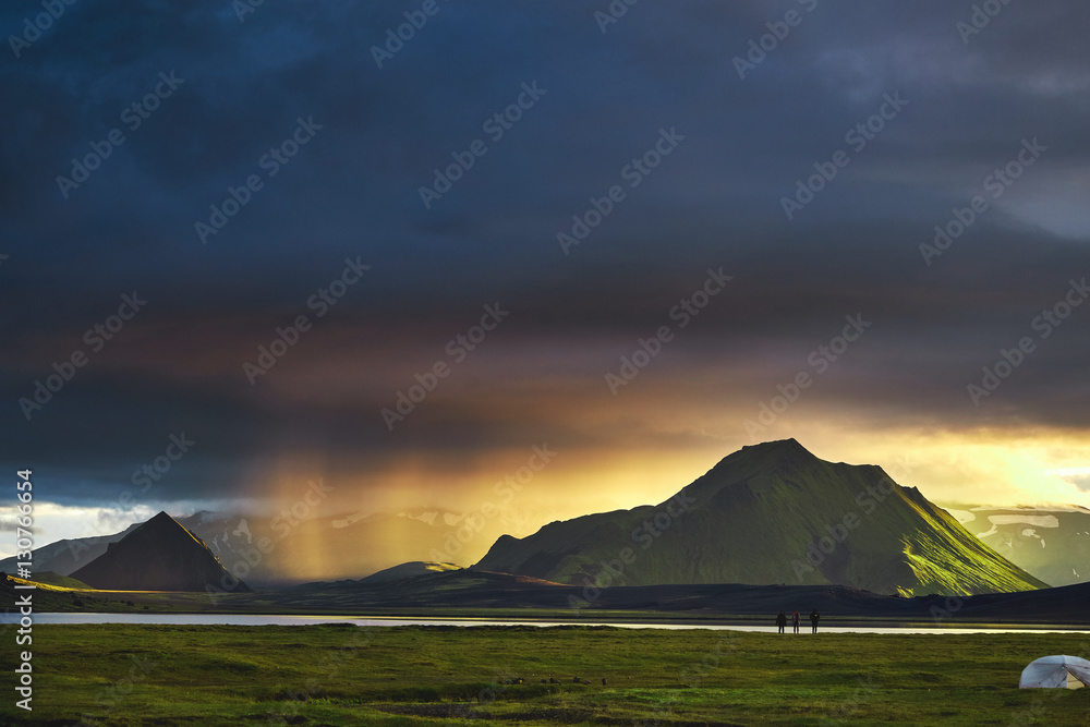 Travel to Iceland. Beautiful Icelandic landscape with mountains, sky and clouds. Trekking in national park Landmannalaugar. Rainy and cloudy Evening in Camping near Alftavatn lake. Tents and hikers in
