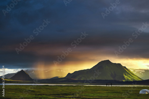 Travel to Iceland. Beautiful Icelandic landscape with mountains, sky and clouds. Trekking in national park Landmannalaugar. Rainy and cloudy Evening in Camping near Alftavatn lake. Tents and hikers in