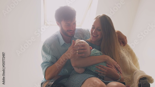 Beautiful happy family mother lulling her baby in a rocking chair father pats on the head of his son and kisses wife. 4k