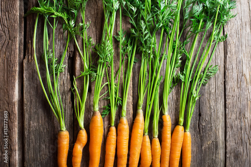 Raw carrot with green leaves on wooden background