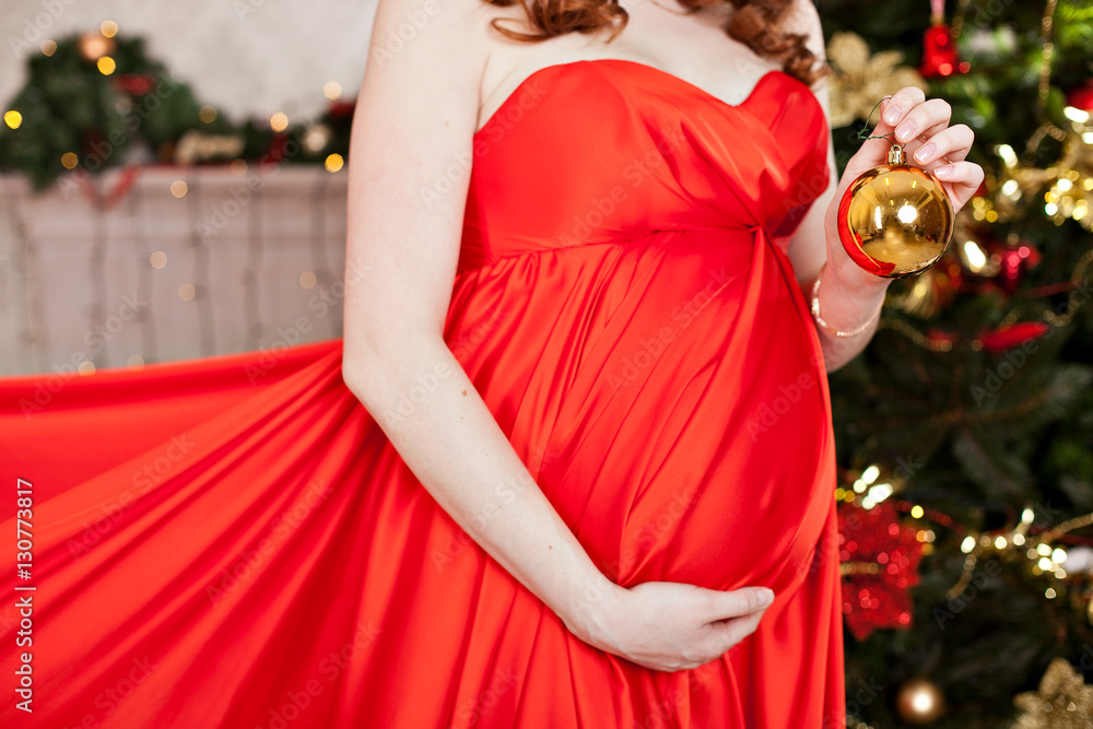 belly of a pregnant woman in a red dress with a New Year's ball