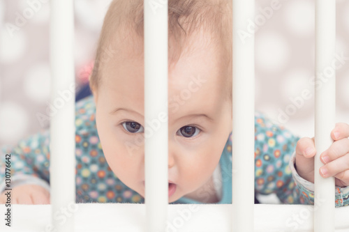 Eight months old baby girl in her bed, looking through the bars
