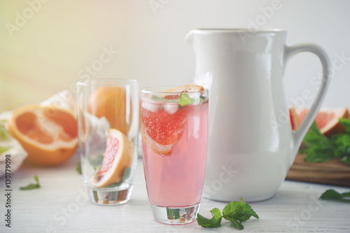 Glass of grapefruit lemonade and jug on white wooden table