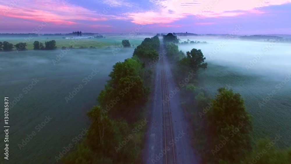 Flying over surreal foggy landscape with railroad tracks at daybreak.
Flying over surreal foggy landscape with railroad tracks at daybreak.