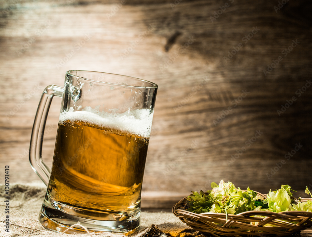 Fototapeta premium Big mug of beer stands on linen cloth with hops