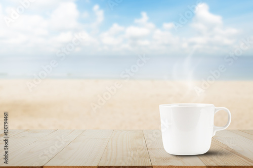 Hot coffee with smoke on wooden table top on blurred beach background