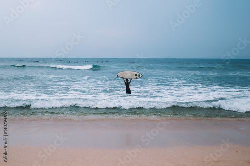 Young boy holds a surfboard above his head in the ocean, Indonesia, Bali