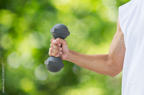 Man wearing sleeveless white shirt holding old dumbbell on blurred green bokeh background, sport exercise concept