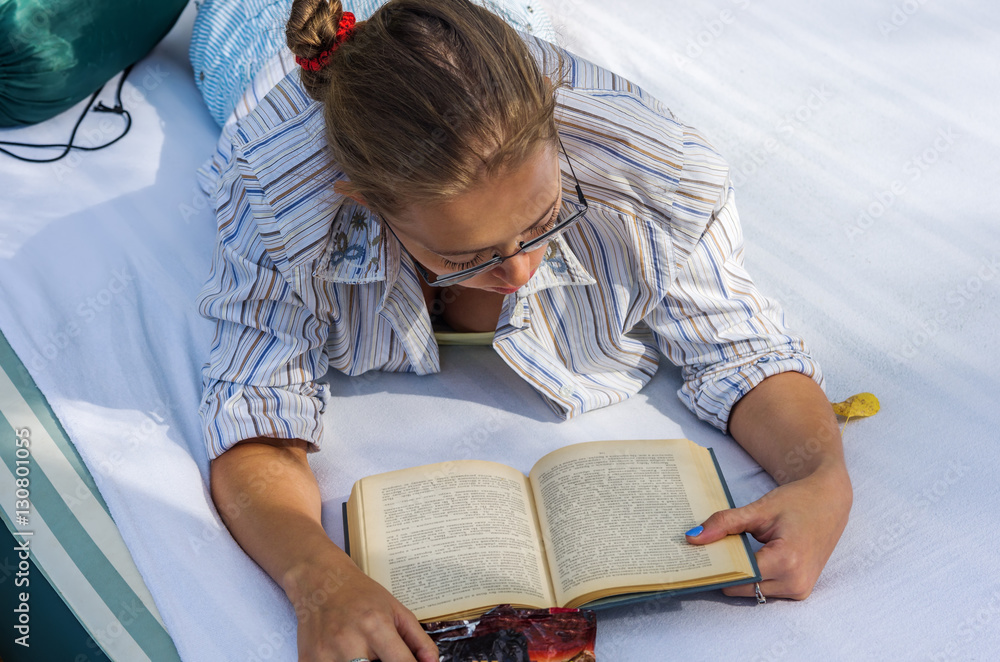 Girl with glasses reading a book, lying on an air mattress Girl with glasses reading a book, lying on an air mattress