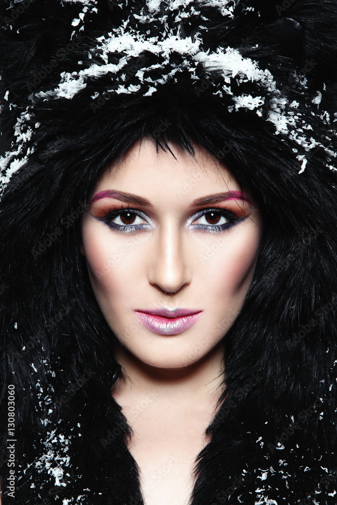 Portrait of young beautiful woman with stylish make-up in fur hat and snowflakes