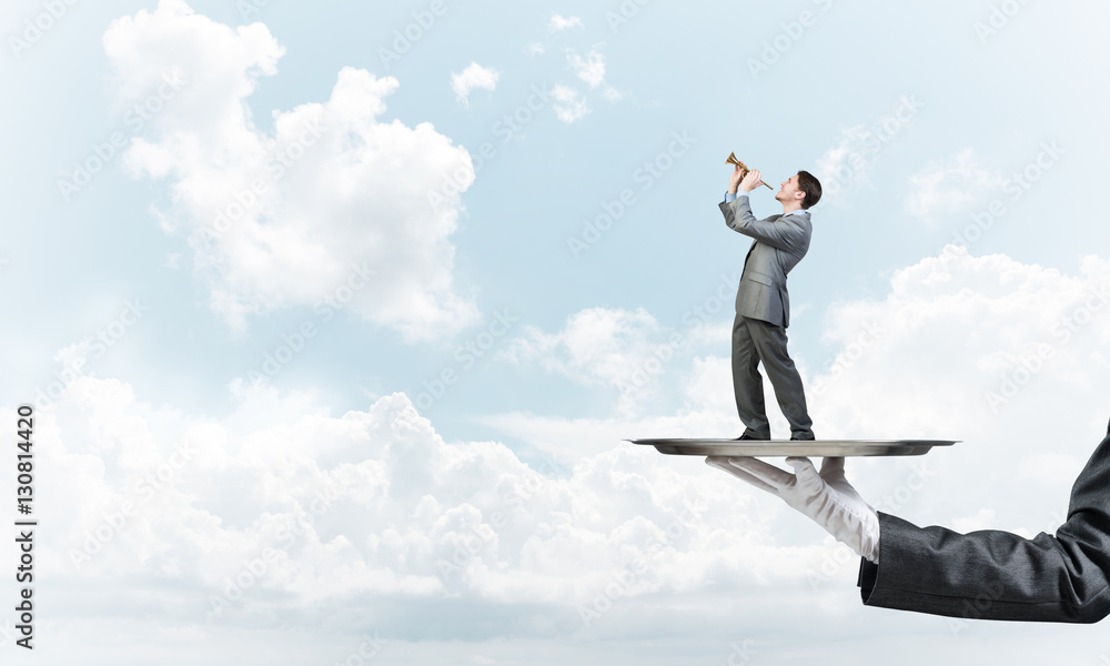 Businessman on metal tray playing fife against blue sky background Businessman on metal tray playing fife against blue sky background