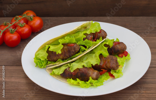 Tortilla with meat wrapped in bacon and herbs. Wooden background