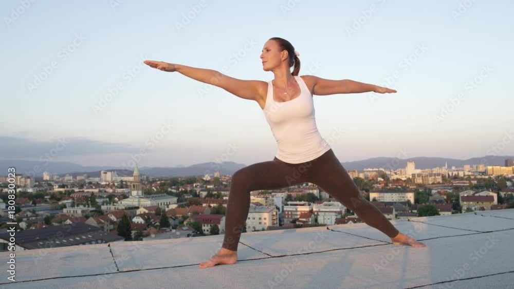 CLOSE UP: Beautiful young girl doing warrior pose on skyscraper at sunrise CLOSE UP: Beautiful young girl doing warrior pose on skyscraper at sunrise