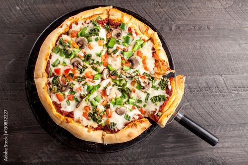 Home made pizza from scratch topped with mushrooms, turkey, kale, peppers, and tomatoes cut on a dark background